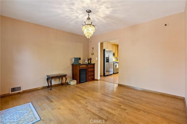 empty room featuring light hardwood / wood-style flooring, beverage cooler, and a notable chandelier