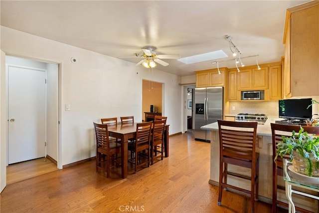 dining room featuring a skylight, ceiling fan, and light wood-type flooring