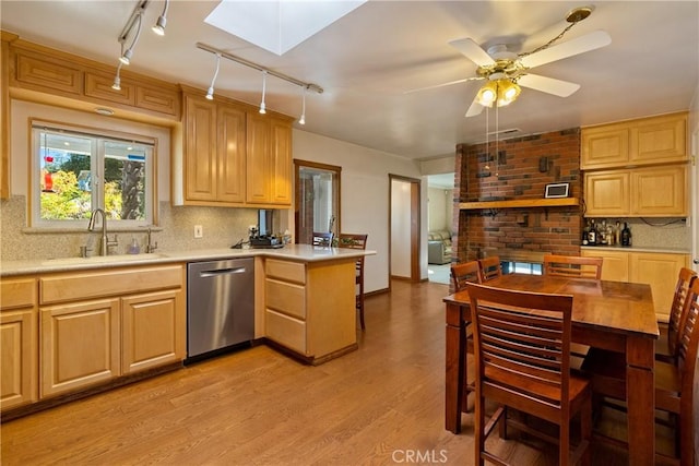 kitchen featuring kitchen peninsula, a skylight, stainless steel dishwasher, sink, and light hardwood / wood-style flooring