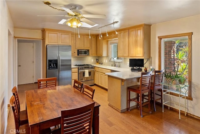 kitchen featuring kitchen peninsula, appliances with stainless steel finishes, decorative backsplash, light brown cabinetry, and light hardwood / wood-style floors