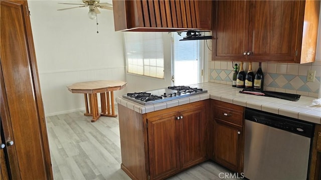 kitchen featuring appliances with stainless steel finishes, backsplash, light hardwood / wood-style flooring, and tile counters