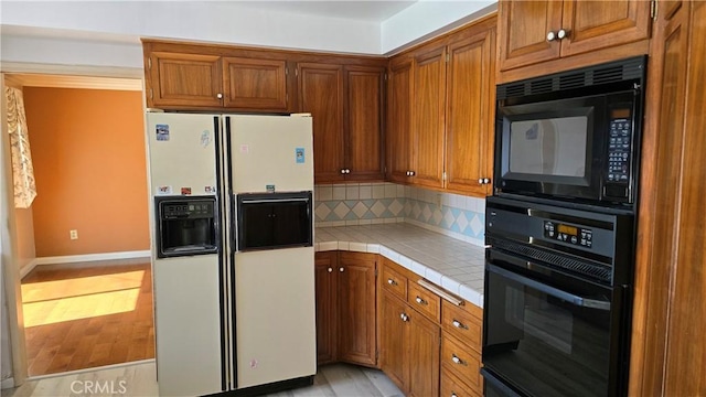 kitchen with black appliances, light hardwood / wood-style floors, tasteful backsplash, and tile countertops