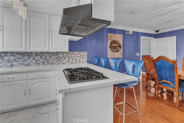 kitchen featuring a breakfast bar area, exhaust hood, white cabinets, light countertops, and stainless steel gas stovetop