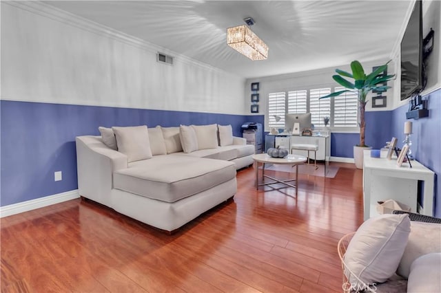 living area with baseboards, wood finished floors, visible vents, and crown molding