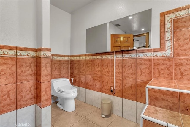 bathroom with tile patterned flooring, toilet, visible vents, tile walls, and wainscoting