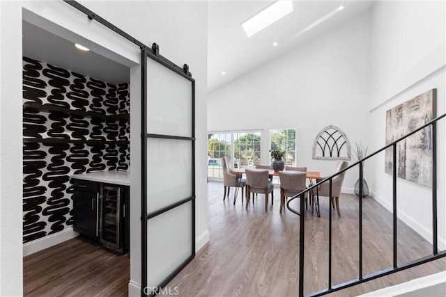 dining space featuring indoor bar, a barn door, hardwood / wood-style flooring, high vaulted ceiling, and wine cooler