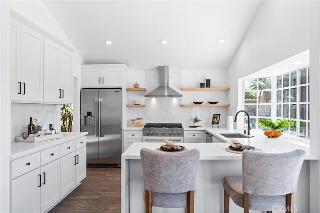 kitchen with high quality appliances, lofted ceiling, wall chimney exhaust hood, kitchen peninsula, and a breakfast bar area