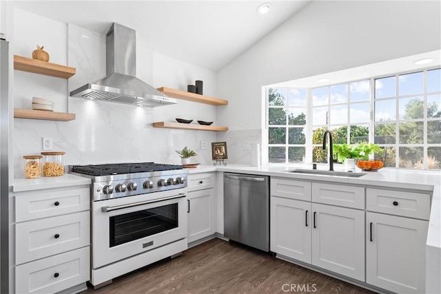 kitchen with sink, wall chimney range hood, lofted ceiling, white cabinets, and appliances with stainless steel finishes