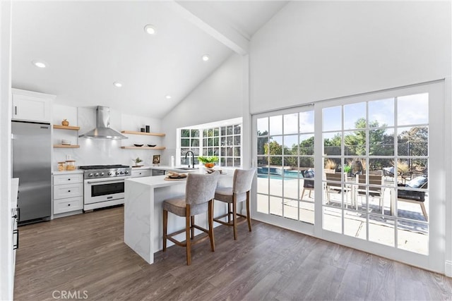 kitchen featuring wall chimney range hood, kitchen peninsula, a breakfast bar, white cabinets, and appliances with stainless steel finishes