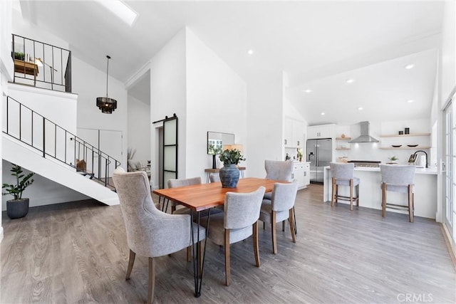 dining area featuring a barn door, light hardwood / wood-style flooring, and high vaulted ceiling