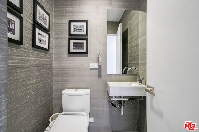 bathroom featuring toilet, tile walls, and sink