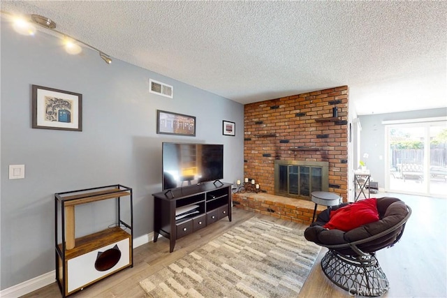 living room featuring a textured ceiling, light wood-type flooring, and a brick fireplace