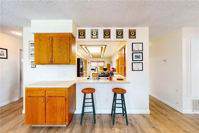 kitchen featuring kitchen peninsula, stainless steel fridge, a kitchen bar, sink, and light hardwood / wood-style flooring