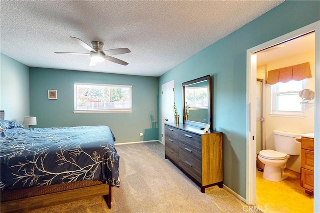 bedroom featuring ceiling fan, light colored carpet, ensuite bathroom, and a textured ceiling