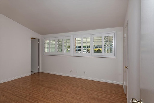 spare room featuring vaulted ceiling and hardwood / wood-style flooring