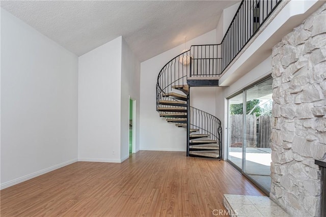 interior space featuring a fireplace, high vaulted ceiling, wood-type flooring, and a textured ceiling