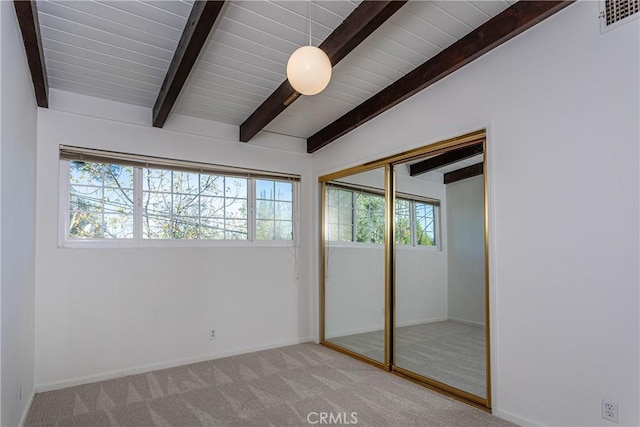 unfurnished bedroom featuring vaulted ceiling with beams, light colored carpet, multiple windows, and a closet