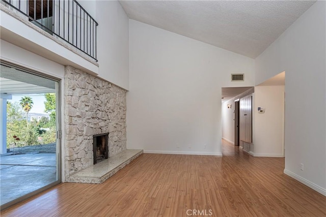 unfurnished living room featuring a stone fireplace, high vaulted ceiling, wood-type flooring, and a textured ceiling