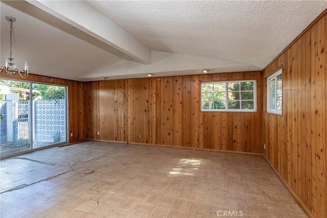 spare room featuring a chandelier, a textured ceiling, and wood walls