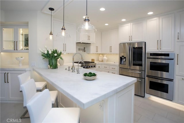 kitchen with white cabinets, hanging light fixtures, appliances with stainless steel finishes, tasteful backsplash, and a breakfast bar area