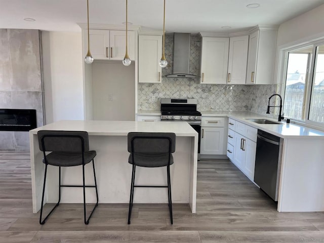 kitchen with sink, a center island, wall chimney range hood, white cabinets, and appliances with stainless steel finishes