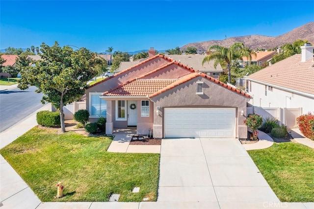 mediterranean / spanish house with a mountain view, fence, concrete driveway, stucco siding, and a front yard