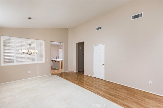 empty room featuring visible vents, a sink, an inviting chandelier, and wood finished floors