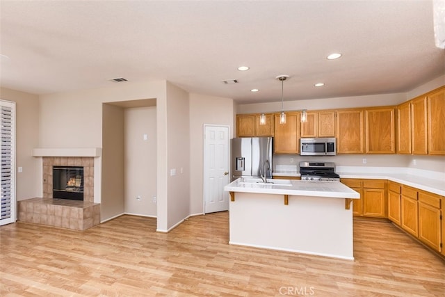 kitchen with a kitchen island with sink, stainless steel appliances, open floor plan, light countertops, and decorative light fixtures