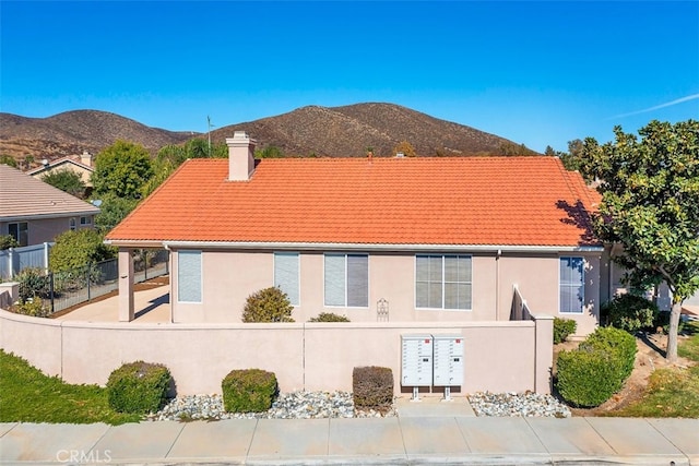 exterior space with a tile roof, a chimney, stucco siding, fence, and a mountain view