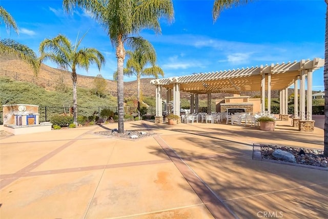 view of patio / terrace with an outdoor stone fireplace, a mountain view, fence, and a pergola