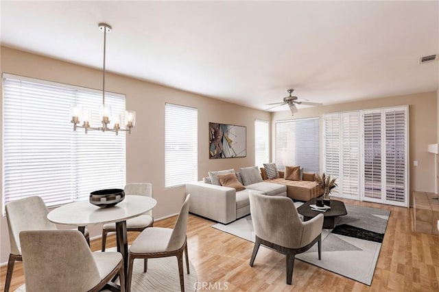 living area with light wood-type flooring, baseboards, visible vents, and ceiling fan with notable chandelier