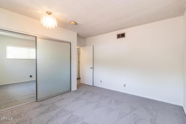 unfurnished bedroom featuring light colored carpet, a textured ceiling, and a closet