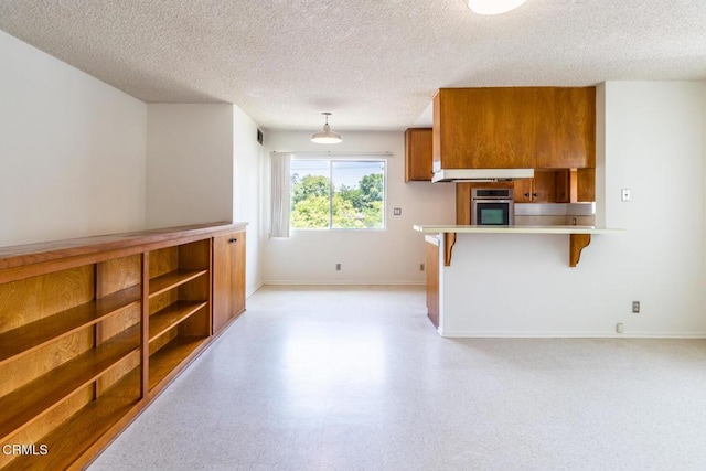 kitchen featuring a breakfast bar, stainless steel oven, a textured ceiling, and decorative light fixtures