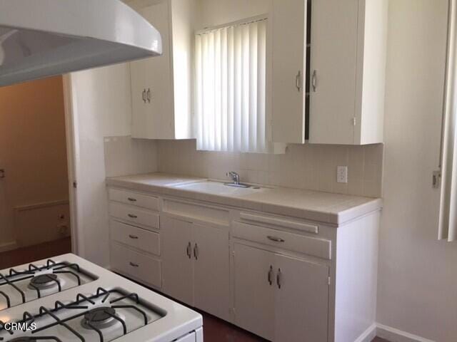 kitchen featuring decorative backsplash, gas range gas stove, sink, and white cabinets