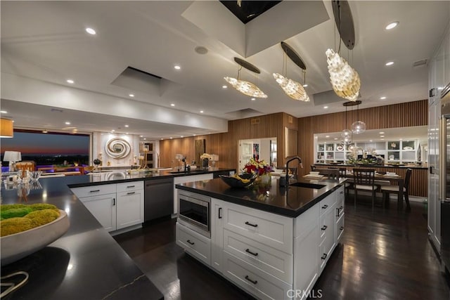 kitchen featuring white cabinets, decorative light fixtures, a center island with sink, and stainless steel appliances