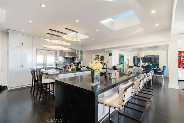 kitchen featuring hanging light fixtures, a kitchen breakfast bar, a spacious island, white cabinets, and exhaust hood