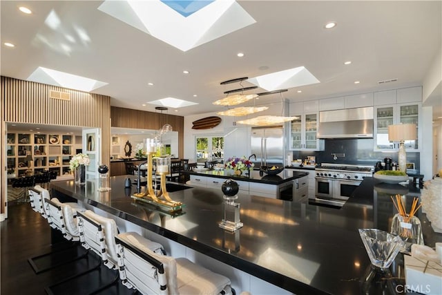 kitchen featuring a skylight, ventilation hood, pendant lighting, a center island with sink, and high end appliances