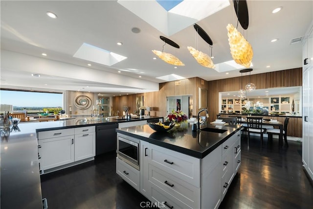 kitchen featuring a skylight, stainless steel microwave, white cabinets, and decorative light fixtures