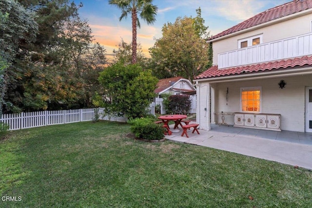 yard at dusk featuring a balcony and a patio