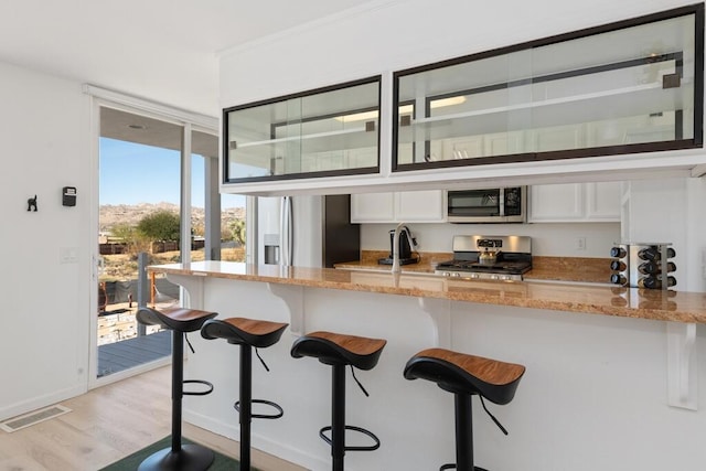 kitchen featuring light stone countertops, white cabinets, light wood-type flooring, and appliances with stainless steel finishes