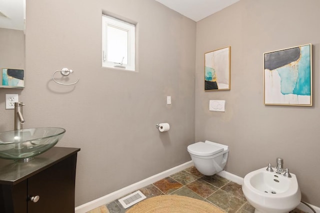 bathroom with a bidet, vanity, and toilet