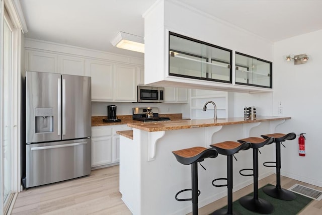 kitchen featuring a kitchen breakfast bar, white cabinetry, light hardwood / wood-style floors, kitchen peninsula, and stainless steel appliances