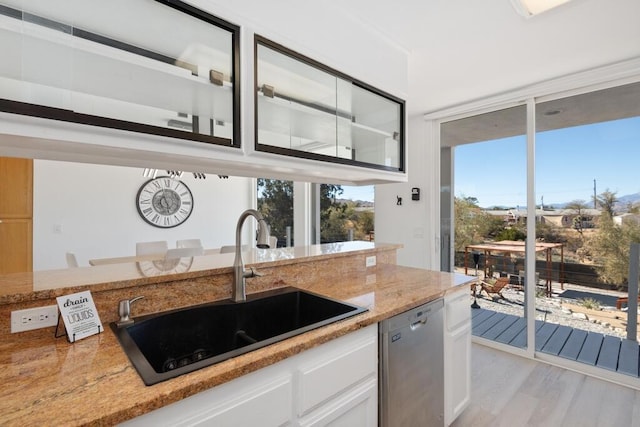 kitchen with sink, stainless steel dishwasher, light hardwood / wood-style floors, light stone counters, and white cabinetry