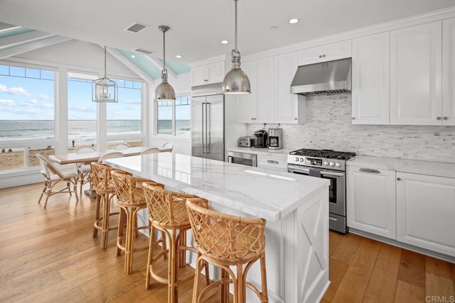 kitchen featuring pendant lighting, appliances with stainless steel finishes, a water view, white cabinets, and exhaust hood