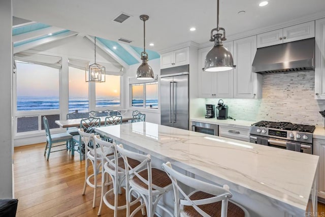 kitchen featuring decorative light fixtures, a kitchen island, stainless steel appliances, light stone countertops, and white cabinets