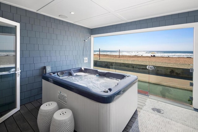 interior space with a water view, a hot tub, and a beach view