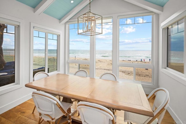 dining area featuring vaulted ceiling with beams, a beach view, baseboards, and wood finished floors