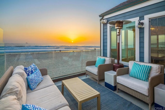 balcony with an outdoor living space, a water view, and a view of the beach