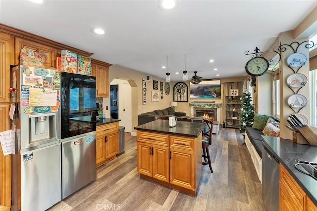 kitchen with appliances with stainless steel finishes, a breakfast bar, ceiling fan, hardwood / wood-style flooring, and a kitchen island