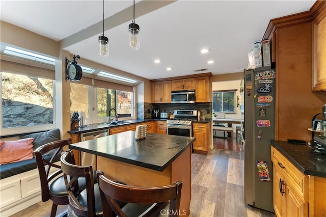 kitchen with sink, light hardwood / wood-style floors, pendant lighting, decorative backsplash, and appliances with stainless steel finishes